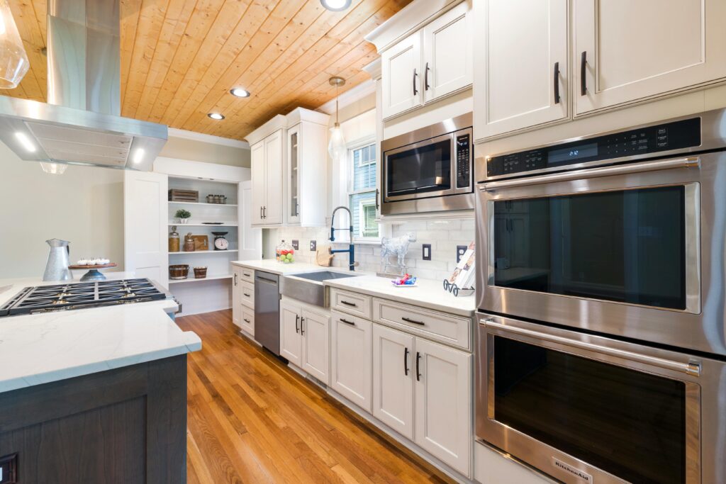 Spacious modern kitchen design featuring white cabinets, wooden floors, and stainless steel appliances.